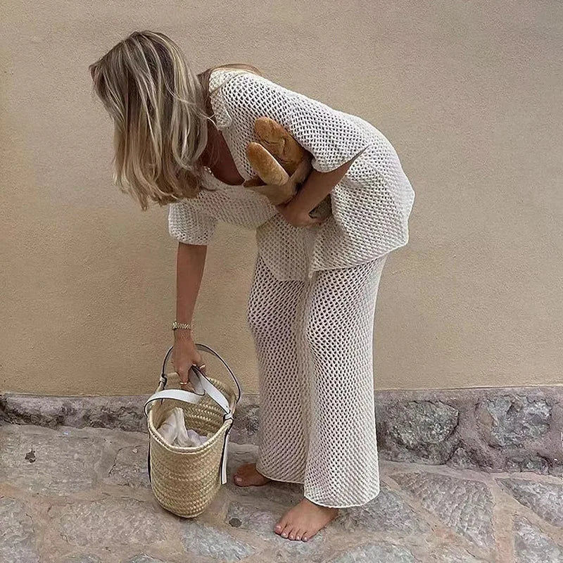 Woman in a textured white outfit holding a bread and a woven basket against a beige wall.