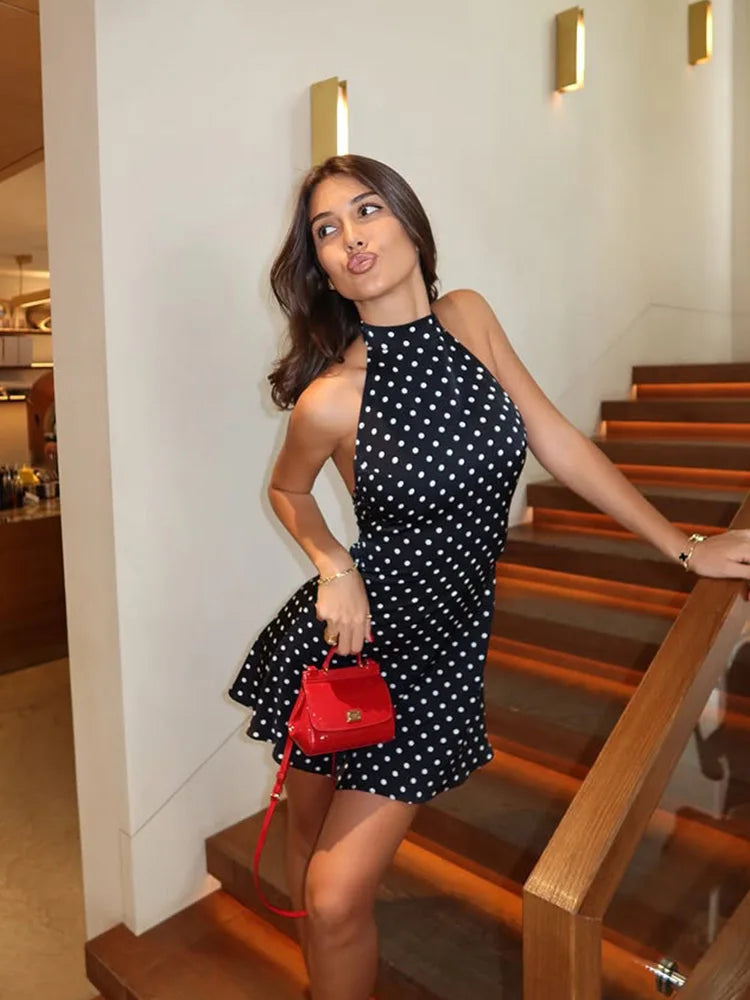 Woman in a black polka dot dress holding a red handbag on a staircase.