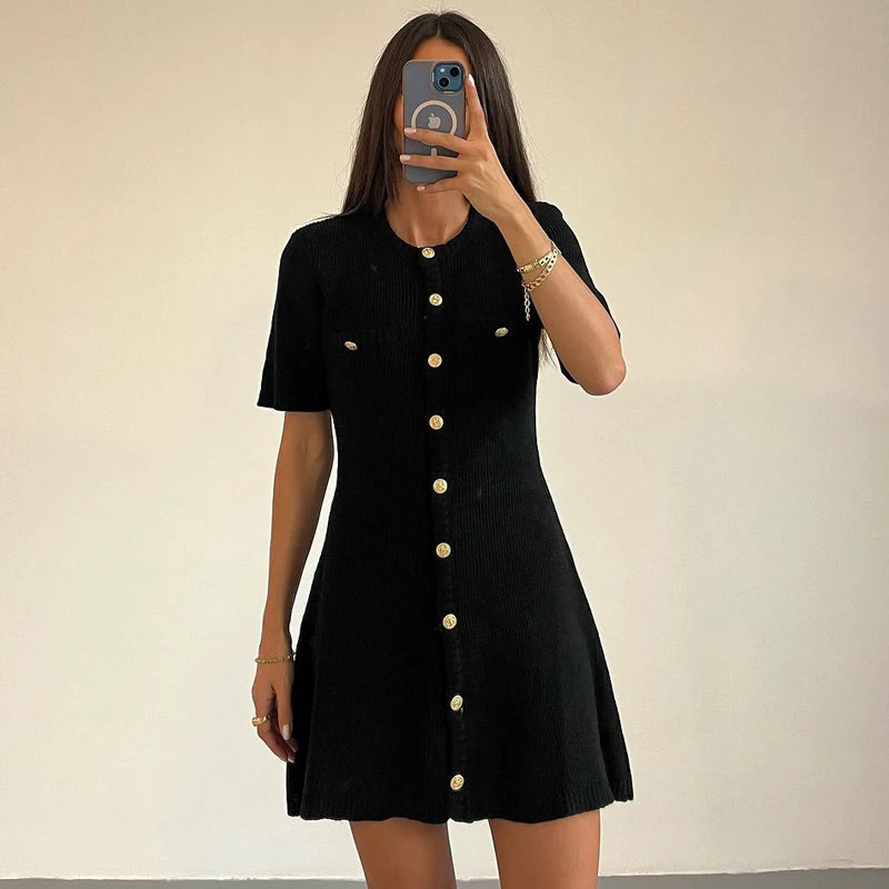 Person wearing a black dress with gold buttons against a plain background
