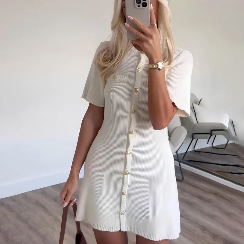 Woman taking a mirror selfie wearing a white ribbed dress in a minimalistic room.