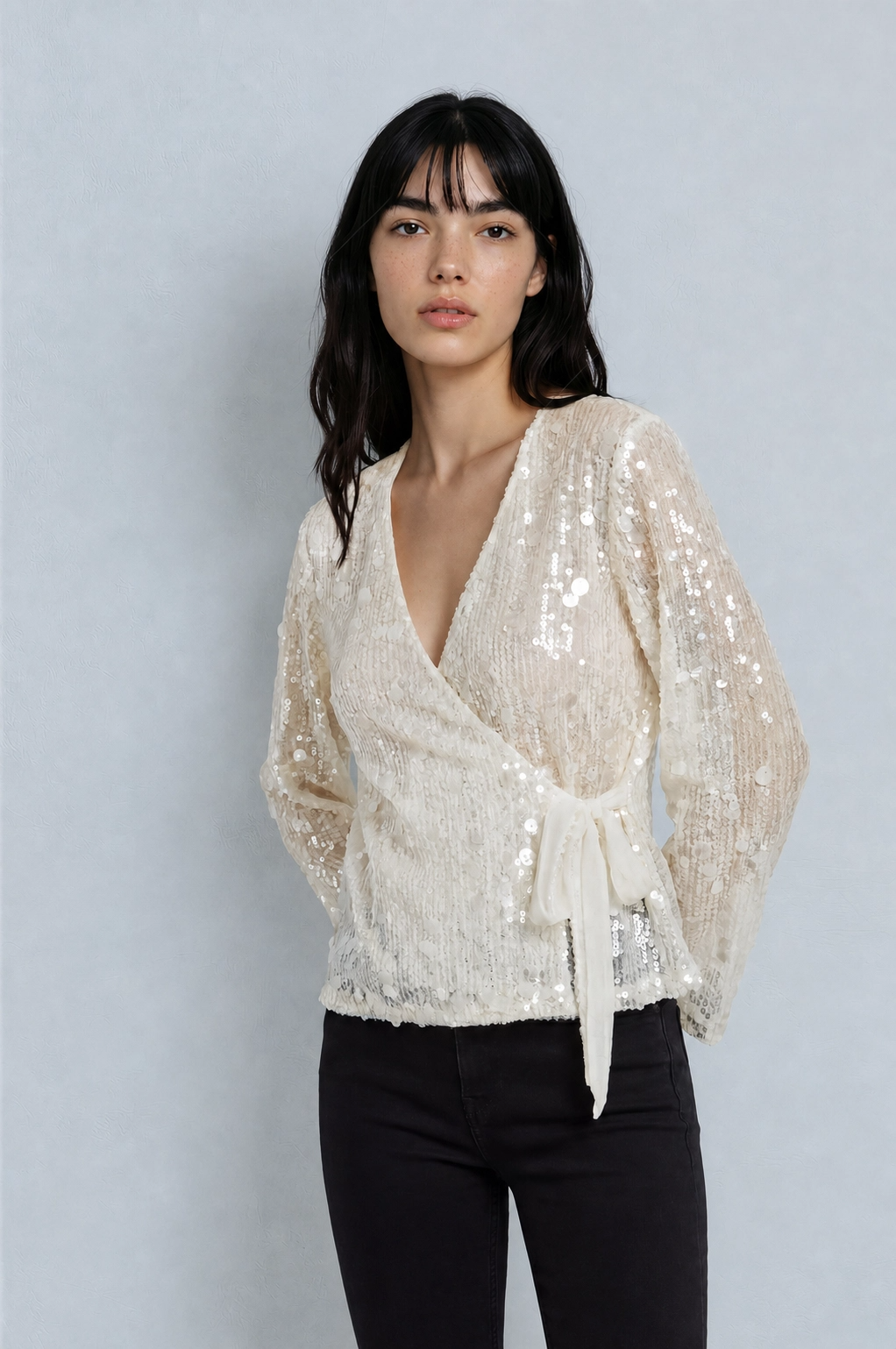 Woman wearing a sparkly white top against a light gray background